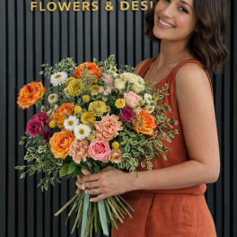 Woman holding a colorful mixed bouquet in front of a flower shop sign