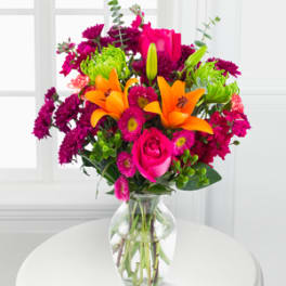 Bouquet of orange lilies, pink roses, and magenta flowers in a glass vase
