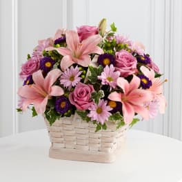 Pink lilies, roses, and daisies arranged in a woven basket
