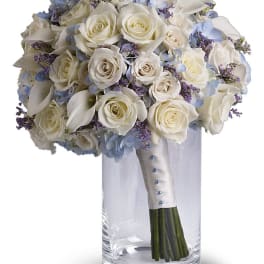 White rose bouquet with blue flowers in a clear glass vase