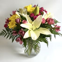 Bouquet of white lilies, pink flowers, and yellow chrysanthemums in a glass vase