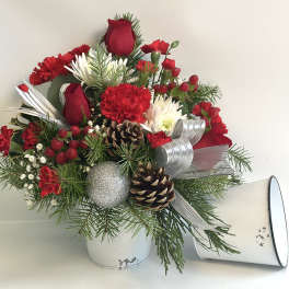 Red and white floral arrangement in a white container with pinecones and ribbon