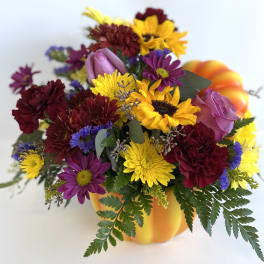 Mixed bouquet in a pumpkin-shaped container with yellow, purple, and burgundy flowers