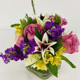 Mixed bouquet with pink roses, white lilies, and purple flowers in a glass vase