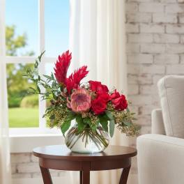 Red floral arrangement in a clear glass vase on a side table