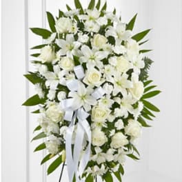 Standing oval spray of white lilies, roses, and mums with a white ribbon on an easel