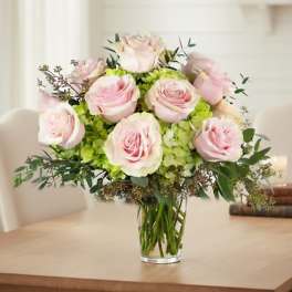 Arrangement of pale pink roses and green hydrangeas in a clear glass vase on a table
