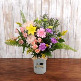 Mixed bouquet of pink, purple, and yellow flowers in a white graduation-themed jar vase