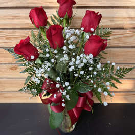 Red roses arranged in a clear vase with white baby's breath and a red ribbon