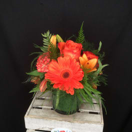 Orange gerbera daisy and roses in a glass vase