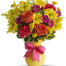 Colorful bouquet of roses, daisies, and carnations in a yellow vase with a pink ribbon