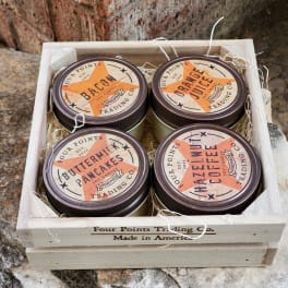 Four scented candles in a wooden crate with straw filler