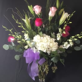 Tall bouquet of pink roses, white lilies, and white hydrangeas in a glass vase