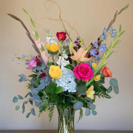 Mixed bouquet of roses, lilies, hydrangea, and blue delphinium in a glass vase