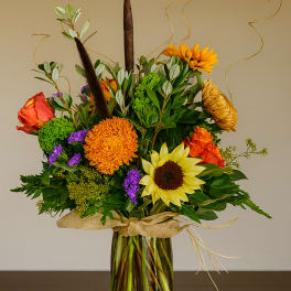 Mixed bouquet in a glass vase with sunflowers, roses, and orange blooms