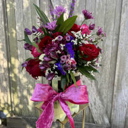 Mixed bouquet of red and purple flowers in a container with a pink bow
