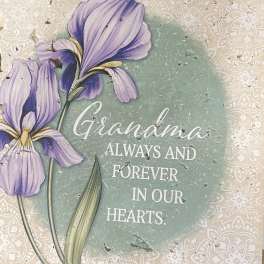 Purple flowers on a memorial plaque reading "Grandma always and forever in our hearts."