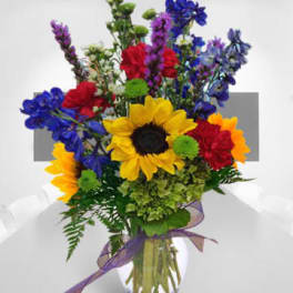 Mixed bouquet with sunflowers, roses, and blue flowers in a glass vase