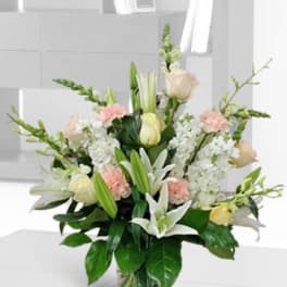 Tall bouquet of white lilies, pale roses, and pink carnations in a glass vase