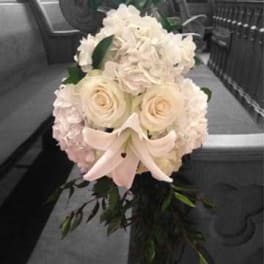 White floral bouquet with roses, lilies, and hydrangeas tied with a pale ribbon