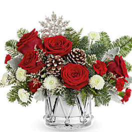 Red roses and white flowers in a clear glass vase with pinecones
