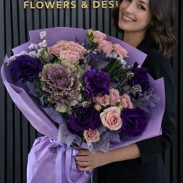 Woman holding a large bouquet of pink and purple flowers wrapped in lavender paper