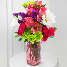 Mixed bouquet of pink roses, white daisies, and purple filler in a pink glass vase