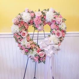 Heart-shaped floral wreath on an easel with pink and white flowers and a white ribbon