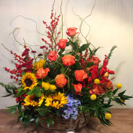 Basket arrangement of roses, sunflowers, and berries with tall curly branches