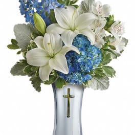 White lilies and blue flowers in a silver vase with a cross
