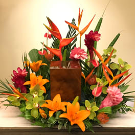 Tropical floral arrangement with orange lilies, orchids, and bird-of-paradise in a square vase