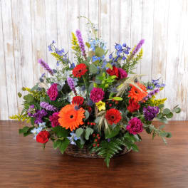 Colorful mixed flower arrangement with red roses and orange gerberas in a wicker basket.