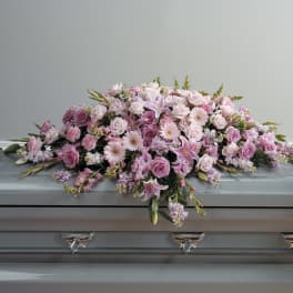 Pink and lavender casket spray with roses, lilies, and other blooms on a gray casket