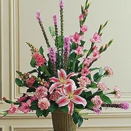 Tall pink floral arrangement with lilies and carnations in a gold-tone container.
