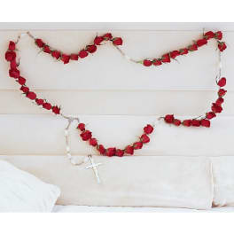 Red rose garland draped across a white upholstered headboard with a cross pendant