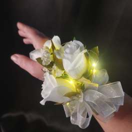 White rose wrist corsage with sheer silver bow and tiny lights on a person’s arm.