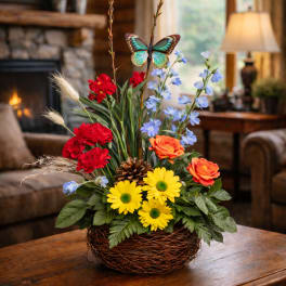 Basket arrangement with red, orange, yellow, and blue flowers and a butterfly pick
