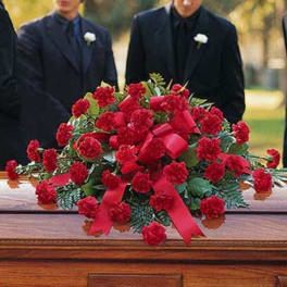 Red carnation casket spray with red ribbon on a wooden casket at a funeral service