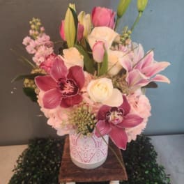 Pink and white mixed flower arrangement with orchids, roses, lilies, and tulips in a patterned vase.