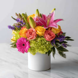 Bright mixed arrangement with pink lilies, roses, green hydrangea, and gerbera daisy in a white vase