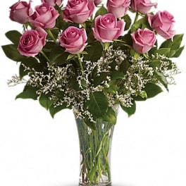 Clear glass vase of lavender roses with white filler flowers.
