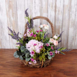 Rustic basket arrangement with pink hydrangea, small pink blooms, peach roses, and purple accent flowers