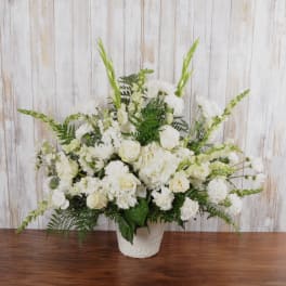 Tall all-white floral arrangement with roses, hydrangeas, carnations, and snapdragons in a white vase