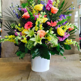 Large mixed bouquet in a white vase with roses, lilies, and bright snapdragons