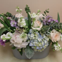 Pastel floral arrangement in a gray container with roses and hydrangeas