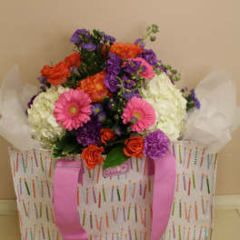 Colorful bouquet in a patterned gift bag with pink ribbon
