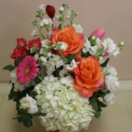 Bouquet of orange and red roses with white blooms in a red vase