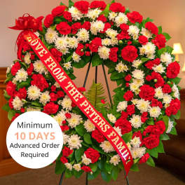 Large standing wreath of red carnations and white chrysanthemums with a red message ribbon