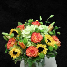 Bouquet of orange roses, yellow sunflowers, and white hydrangeas in a glass vase