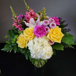 Mixed bouquet of yellow roses, pink blooms, and white hydrangea in a glass vase